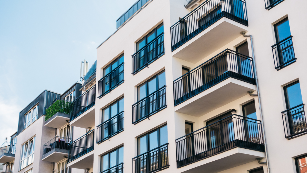 Modern apartment building exterior with multiple balconies and large windows under a clear sky.