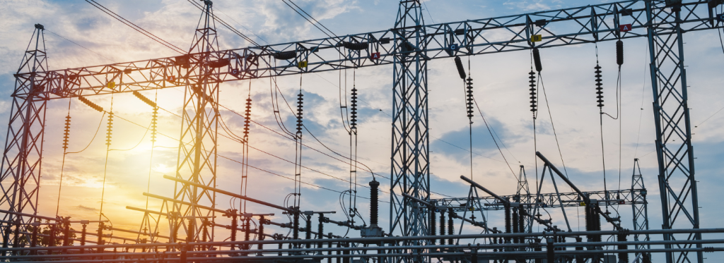 Electrical substation infrastructure with metal towers, power lines, and insulators set against a cloudy sky during sunset.