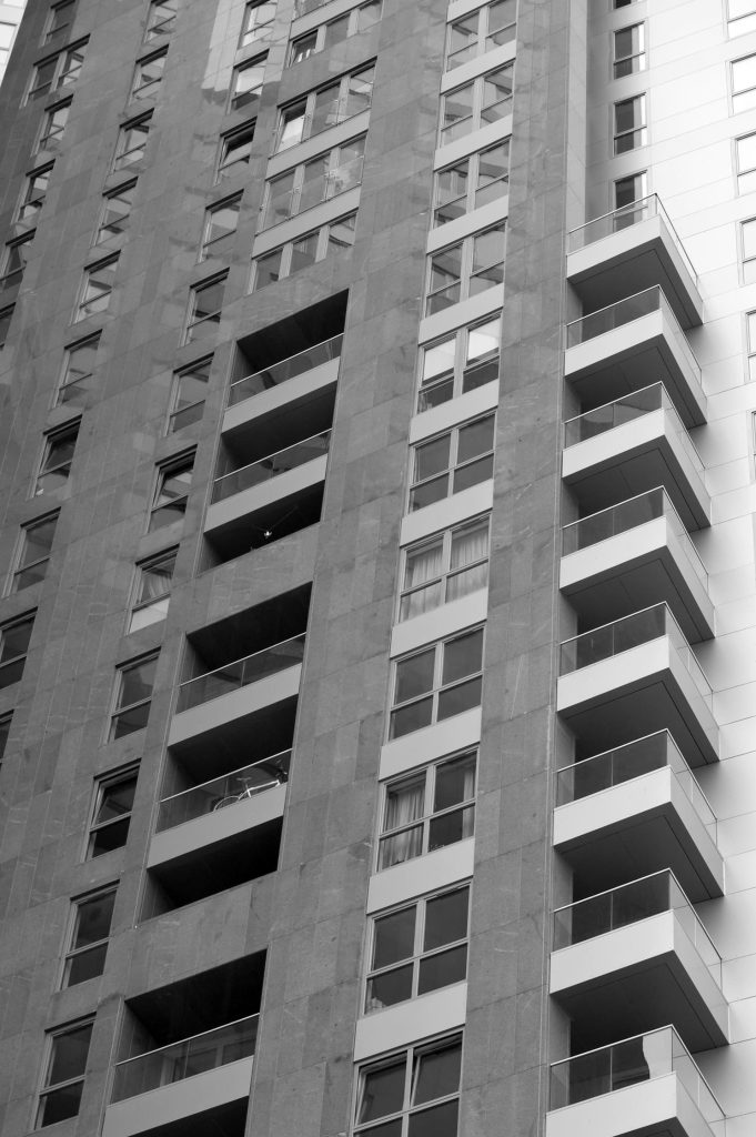 Black and white photo of a modern high-rise building with balconies and large windows, shot from a low angle.