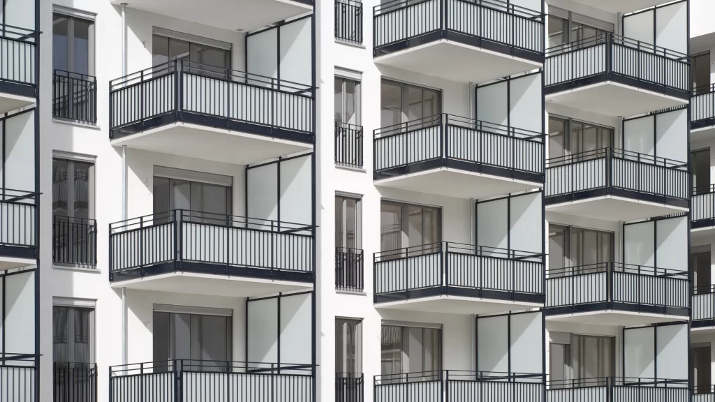 Modern apartment building with multiple balconies featuring black railings and floor-to-ceiling windows on a white facade.