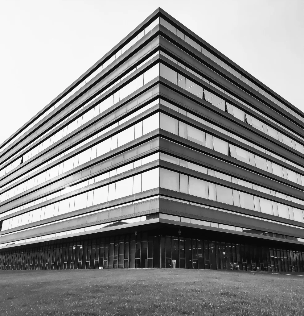 A modern, multi-story office building with horizontal lines and large windows, photographed from a low angle in black and white.