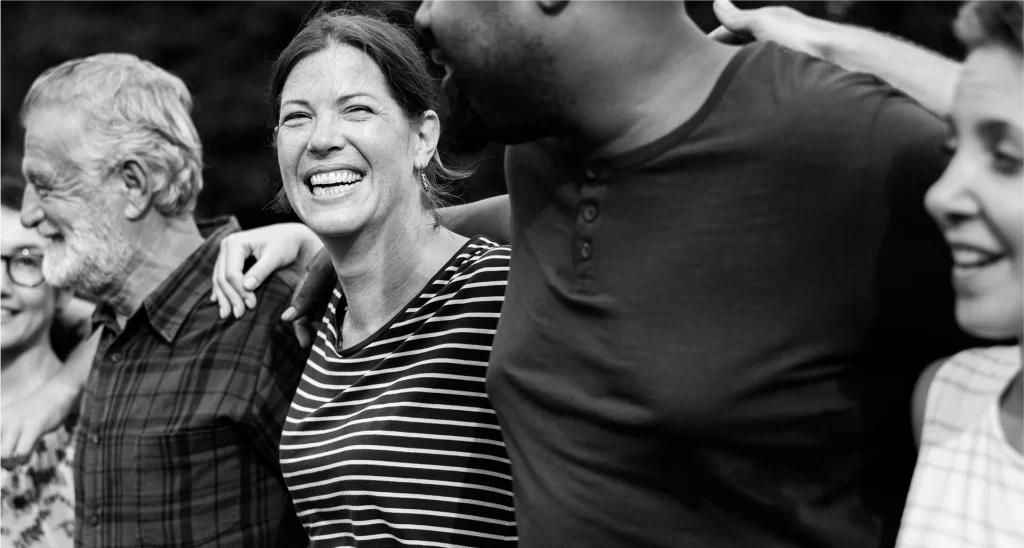 A group of people standing close together outdoors, arms around each other's shoulders, smiling and interacting.