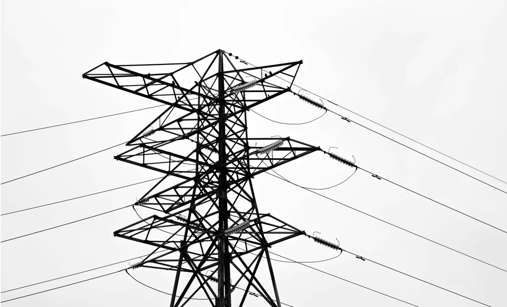 A tall metal electricity pylon with several power lines extending outward, set against a plain, overcast sky.
