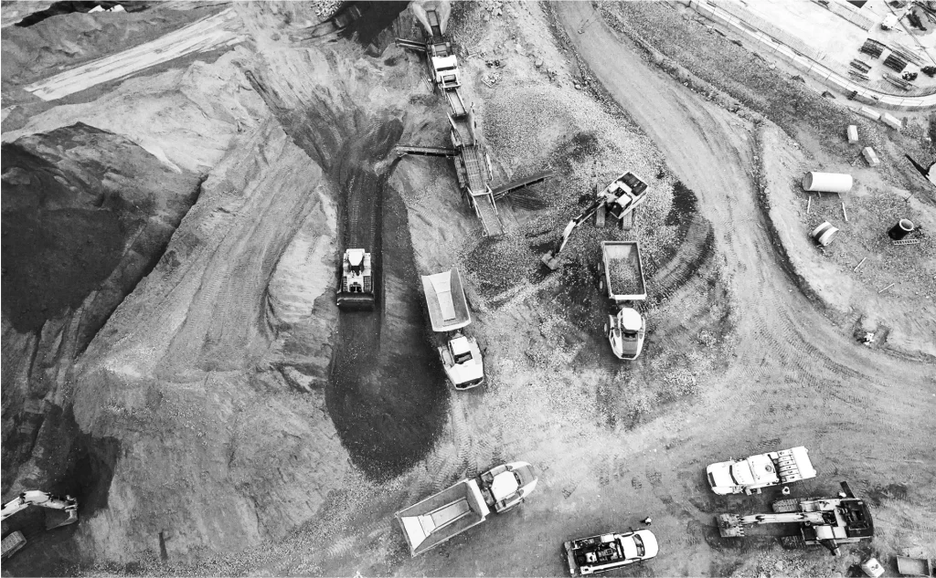 Aerial view of a construction site with trucks, excavators, and machinery working on dirt and gravel piles.