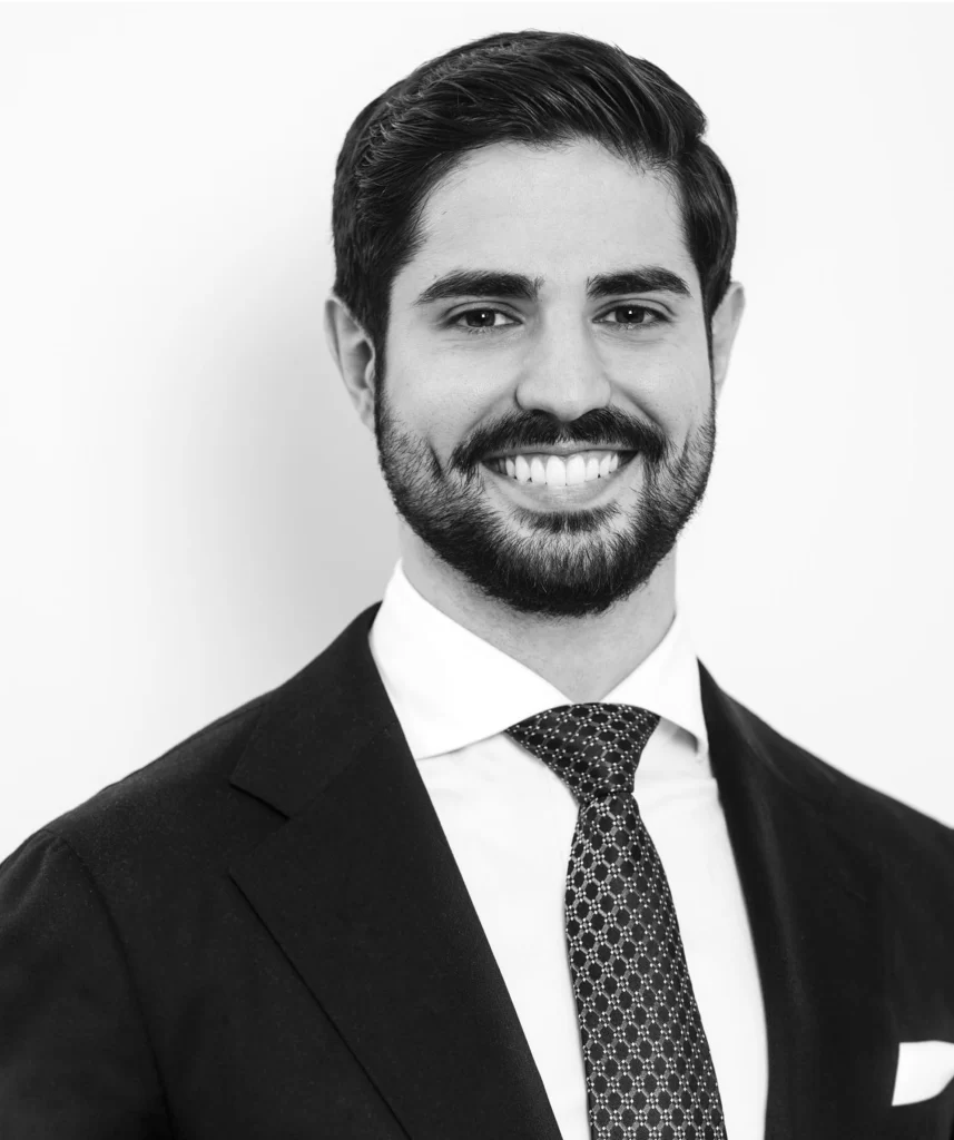A man in a suit and tie smiles at the camera against a plain white background.